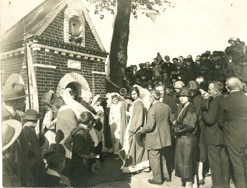 Photographie noir et blanc d'une procession devant une chapelle. Quelques ecclésiastiques et des jeunes filles vêtues d'un long manteau et coiffées d'une voilette se regroupent devant la foule de pélerins.