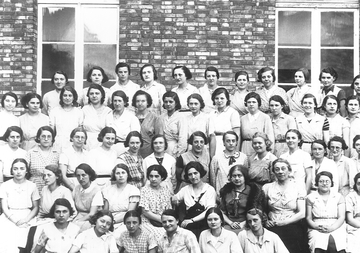 Photographie noir et blanc montrant un groupe de jeunes filles réunies sur une photographie de classe et entourant leurs professeurs.