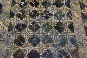 Photo représentant des carreaux disposés en diagonale pour former un damier. Les carreaux clairs sont historiés avec un motif floral et les carreaux foncés sont noirs.